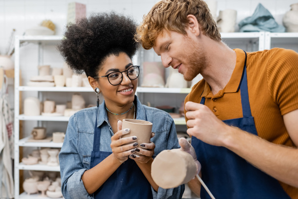 happy interracial couple molding clay cups during date in pottery studio  - Foto, Imagen