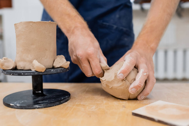 Vista ritagliata di scultore prendere argilla vicino tazza in laboratorio di ceramica  - Foto, immagini