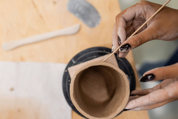 Vista dall'alto dell'artigiana afro-americana che produce prodotti in ceramica con bastone di legno in studio di ceramica  - Foto, immagini