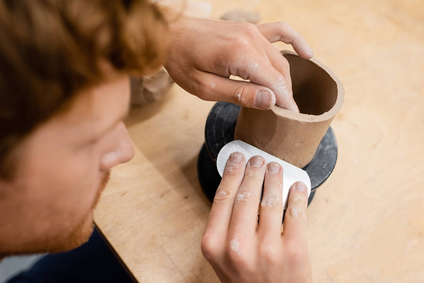 Wazig man holding tool tijdens het maken van keramische sculptuur in aardewerk studio  - Foto, afbeelding