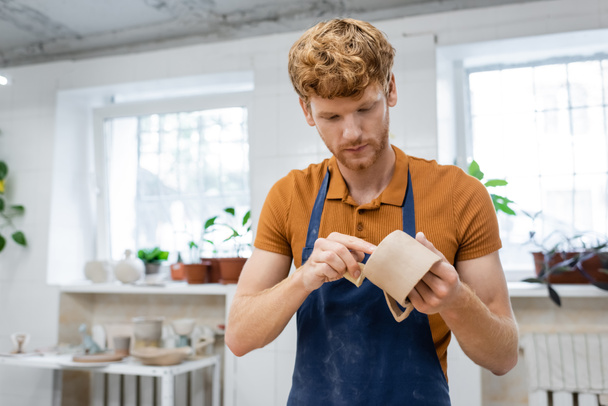 Redhead artisan dans tablier fabrication tasse en céramique en atelier de poterie  - Photo, image