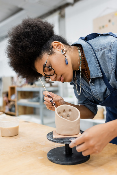 Young african american craftswoman forming clay with wooden stick in pottery workshop  - 写真・画像