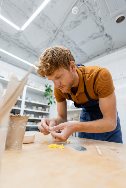 Junge Kunsthandwerkerin in Schürze hält Töpferwerkzeug in Werkstatt  - Foto, Bild