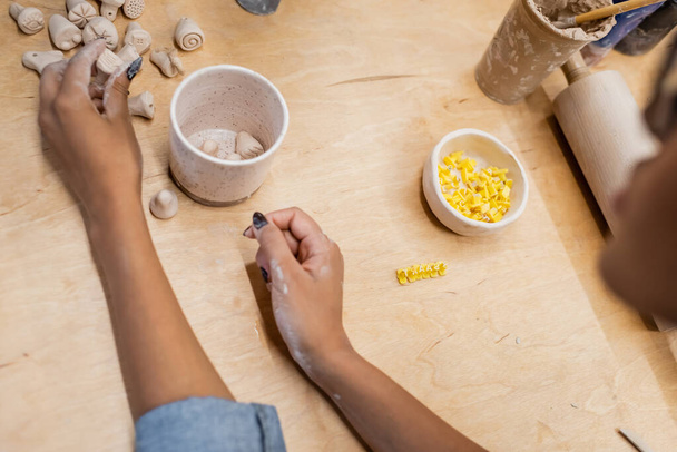 Vista recortada del maestro afroamericano sosteniendo escultura de arcilla cerca de la mesa en taller de cerámica  - Foto, Imagen