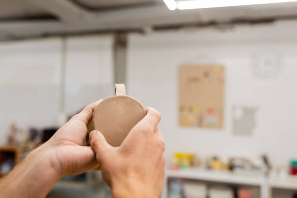 Cropped view of craftsman holding clay cup in blurred pottery workshop  - Photo, Image