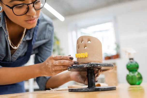 Giovane maestro afroamericano in occhiali che fa scultura in argilla in laboratorio di ceramica  - Foto, immagini