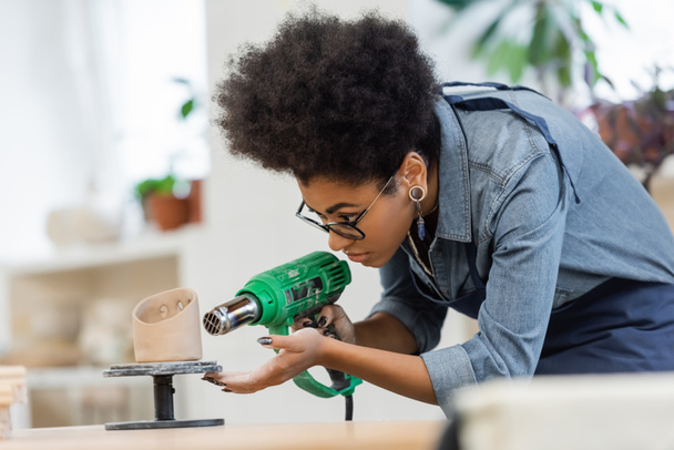 Afroamerikanische Kunsthandwerkerin in Schürze trocknet Keramik-Skulptur in Werkstatt  - Foto, Bild