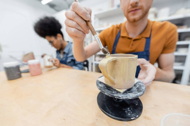 Размытая картина человека на керамической чашке рядом с африканской американской подругой в керамической студии  - Фото, изображение