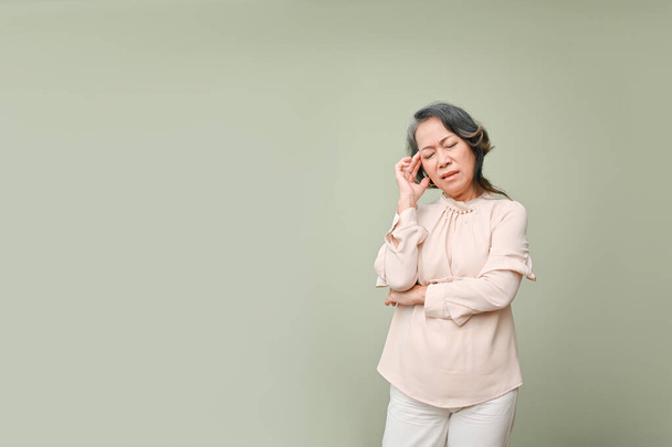 Müde und gestresste Asiatinnen der 60er Jahre in lässiger Kleidung berühren ihre Stirn, die Augen geschlossen, leiden unter Migräne oder Kopfschmerzen und stehen vor isoliertem grünem Hintergrund. Kopierraum für Ihren Text  - Foto, Bild