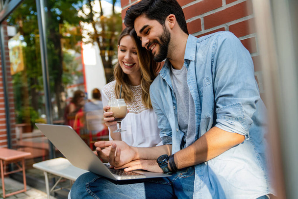 Feliz joven pareja sentada en la cafetería sonriendo, mirando a la pantalla del ordenador portátil, pasar tiempo con placer, beber café. - Foto, Imagen