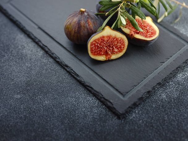 fresh ripe figs fruit and olive branch on dark table. mediterranean food concept - Foto, afbeelding