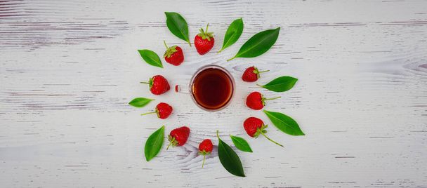 Świeże truskawki organiczne i czarna herbata w szklanym kubku, na białym tle. Wegetariańska koncepcja zdrowej żywności. - Zdjęcie, obraz