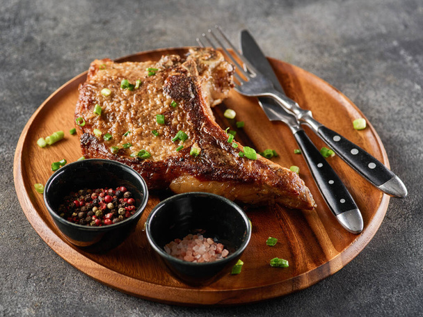 Grilled pork chop on grey plate sprinkled with green onions on the wooden plate, grey background - Photo, Image