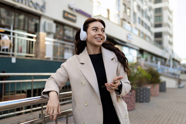 young stylish woman listening to music on headphones with a big smile on her face outside the office. - Photo, Image