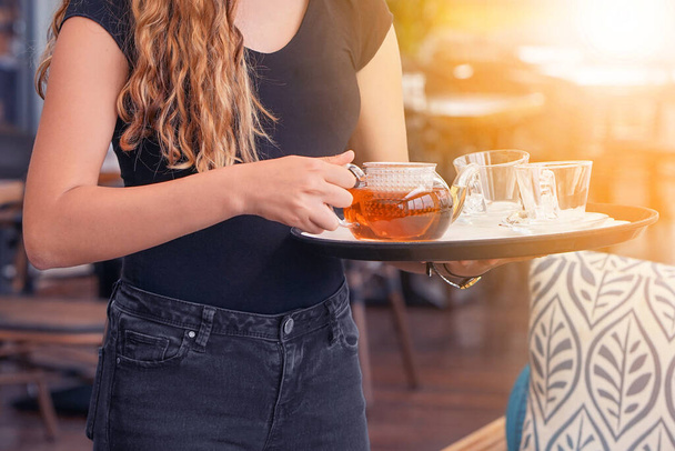 Waitress holding tray with cup of tea and tea glass teapot. Concept of maintenance and service - Φωτογραφία, εικόνα