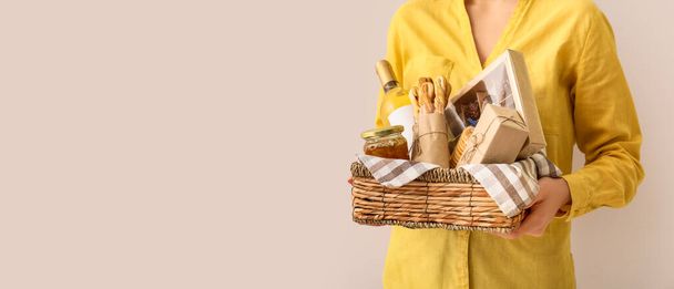 Woman holding gift basket with products on light background with space for text - Photo, Image