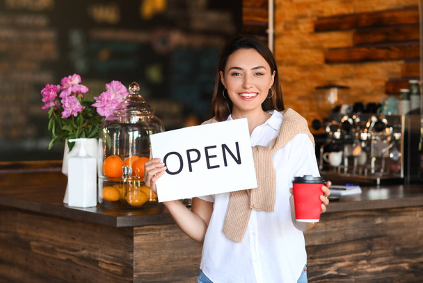 Geschäftsinhaberin mit Eröffnungsschild und Tasse Kaffee in ihrem Café - Foto, Bild