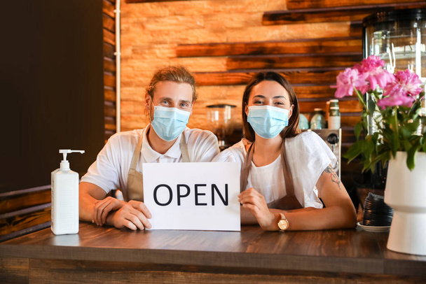 Gli imprenditori con maschere mediche e segno di apertura a tavola nel loro caffè - Foto, immagini