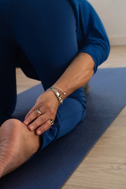 close up yogaleraar gekleed in blauw raakt haar enkels tijdens het stretchen. - Foto, afbeelding