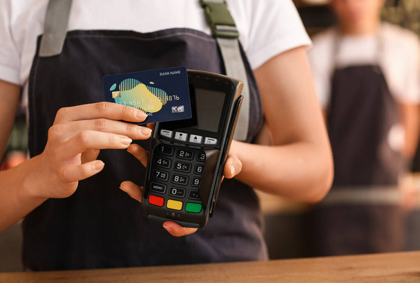 Молодая бариста с кредитной картой и платёжным терминалом в кафе, крупным планом - Фото, изображение