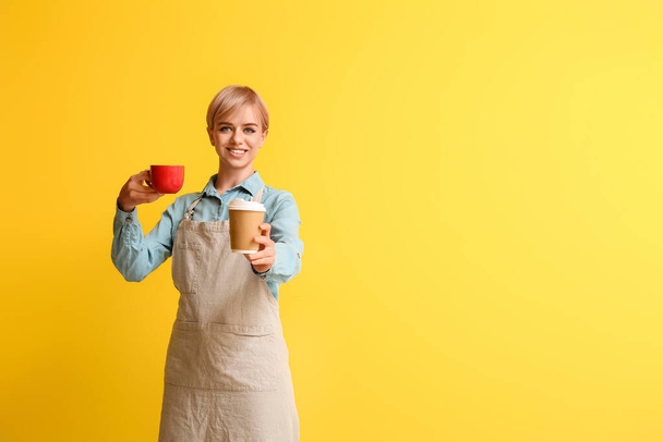 Female barista with cups of coffee on yellow background - Fotó, kép