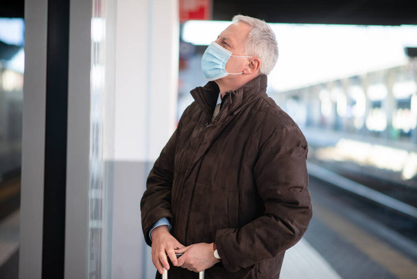 Masked senior businessman waiting for the train, covid and coronavirus mobility concept - Foto, afbeelding