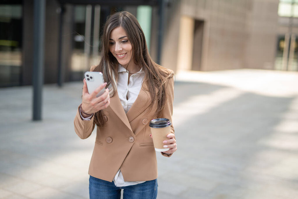 Detail of a young business woman using her smartphone while drinking coffee - Foto, immagini
