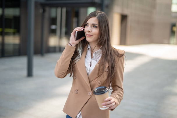 Young businesswoman talking on the phone in a city street while drinking coffee - Foto, Bild