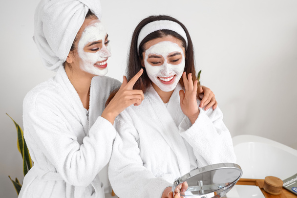 Belles jeunes femmes avec masques faciaux appliqués dans la salle de bain - Photo, image