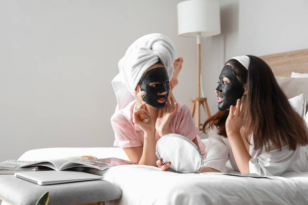 Hermosas mujeres jóvenes con lámina de carbón activado máscaras faciales en el dormitorio - Foto, imagen