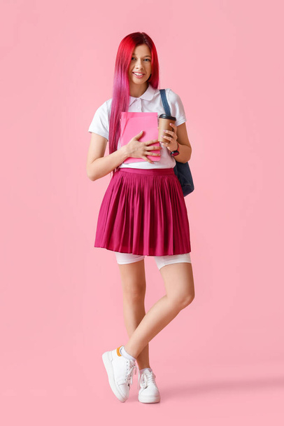 Jonge vrouwelijke student met helder ongewoon haar en koffie op roze achtergrond - Foto, afbeelding