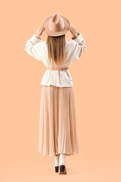 Beautiful fashionable young woman in hat, skirt and knitted sweater on beige background, back view - Fotó, kép