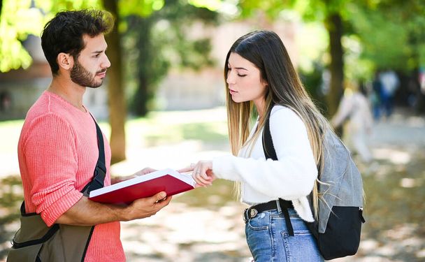 Two students, male and female, talking outdoor in a college park while holding book - Fotografie, Obrázek