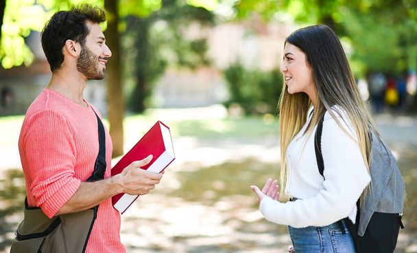 Two students, male and female, talking outdoor in a college park while holding book - Foto, Imagen