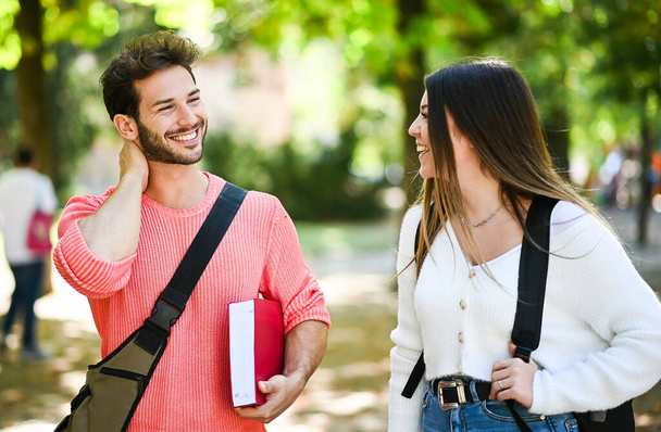 Two students, male and female, talking outdoor in a college park while holding book - Foto, imagen