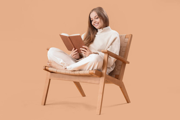 Молодая женщина читает книгу в кресле на бежевом фоне - Фото, изображение
