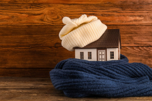ダークウッドの背景にニット帽とスカーフ付きの家モデル。暖房コンセプト - 写真・画像
