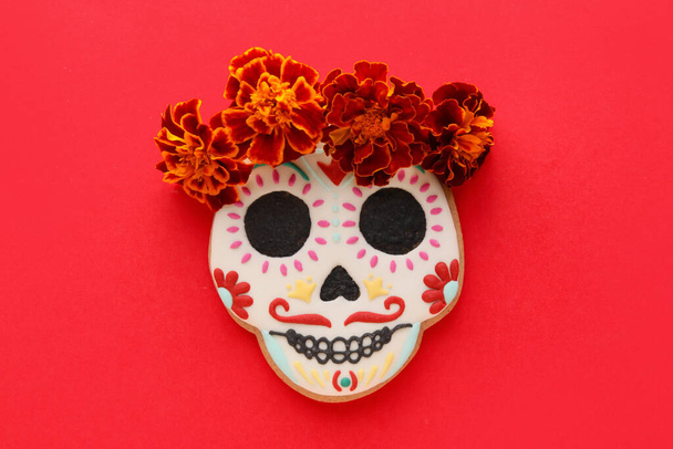 Skull shaped cookie with marigold flowers on red background. El Dia de Muertos - Photo, Image