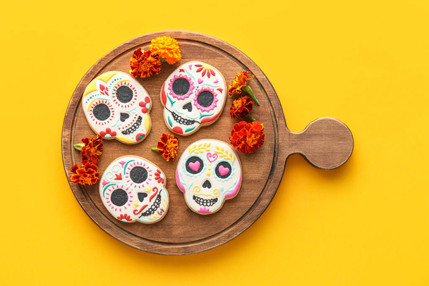 Tábla koponya alakú cookie-k és virágok sárga alapon. El Dia de Muertos-ban. - Fotó, kép