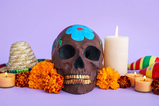 Painted skull for Mexico's Day of the Dead (El Dia de Muertos), flowers, candles and sombrero hat on lilac background - Photo, Image