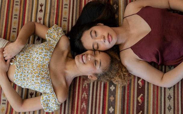 Sensuele multiraciale vrouwelijke paar in kleurrijke kleren liggen oog in oog, bovenaanzicht van paar liggend op de vloer van het huis met gesloten ogen. - Foto, afbeelding