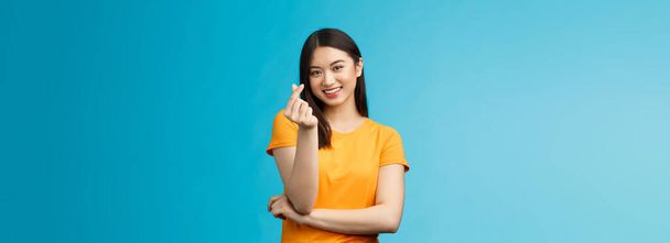 Cheerful cute asian woman dark short haircut, show korean heart sign with fingers, smiling joyfully, express sympathy and caring feelings, confess love stand blue background, grinning upbeat. - Photo, Image