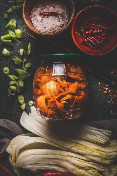 Fermented chinese cabbage marinated in hot chili sauce, kimchi,  in glas jar on rustic background with ingredients. Top view - Foto, Bild