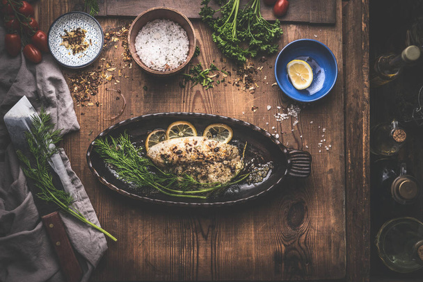 Fish fillet with lemon and  herbs in backing pan on rustic kitchen table background with ingredients. Top view - Fotoğraf, Görsel
