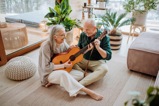 Senior couple playing on guitair, sitting in a cozy living room and enjoying autumn day. - Fotó, kép