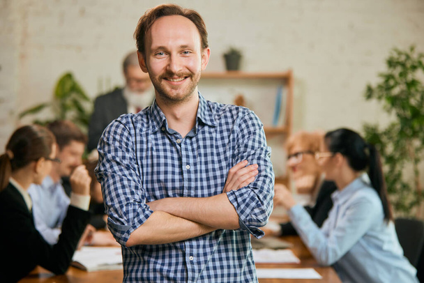 At business meeting. Portrait of young and successful businessman. Happy confident man looking at camera and smiling. Concept of business, teambuilding, finance, success and career - Foto, Bild