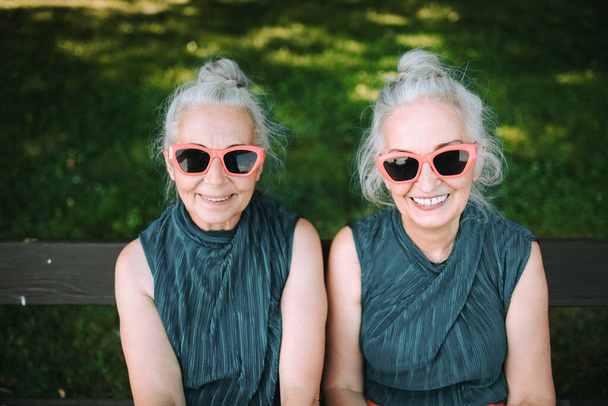 High angle view of happy senior women, twins in same clothes, smiling and posing in a city park. - Φωτογραφία, εικόνα