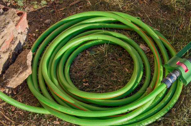 un tubo verde per annaffiare arrotolato formando un cerchio su un piano di terra e pietre - Foto, immagini