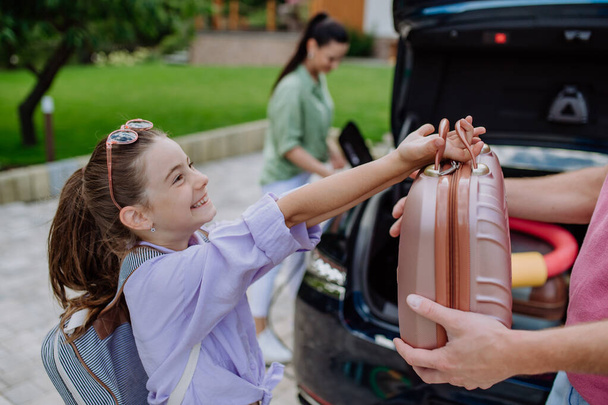 Happy mother holding power supply cable and charging their electric car, rest of family putting suitcases in a car trunk, preparating for holidays. - Foto, Imagen