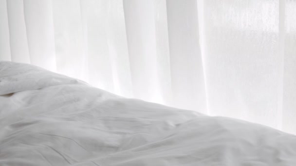 белый занавес с солнечным светом через окно с кроватью и белым бельем постельное белье в уютной спальне в раннее утро время, фон естественный - Кадры, видео